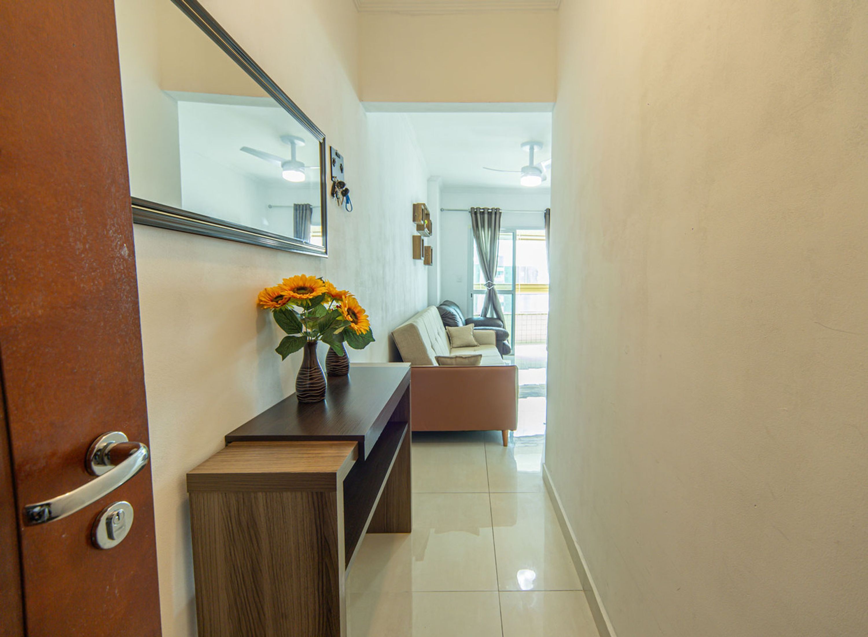 A hallway with a wooden bench, a vase with sunflowers, a mirror, and a door with a handle.