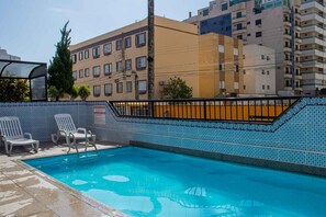 A swimming pool with tiled walls and a metal railing, surrounded by white lounge chairs. - Apartamento Pet Friendly c Garagem a 400m da Praia (Praia Grande)