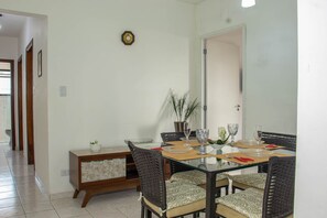 A dining area with a glass table, wicker chairs, and a wooden sideboard. - Apartamento Pet Friendly c Garagem a 400m da Praia (Praia Grande)