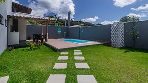 A backyard with a swimming pool, a covered patio, and a stone pathway. - Pedra DO MAR Apto Perto da Praia de Taperapuan (Porto Seguro)