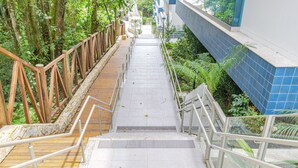 Eine Treppe mit Metallgeländern, umgeben von Grünpflanzen und einer Steinmauer auf der einen Seite sowie einer Kachelwand auf der anderen.
