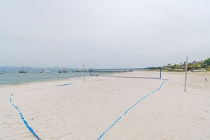 Een beachvolleybalveld met een net, omringd door zand en met uitzicht op de zee, met boten op de achtergrond.