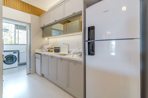 Een moderne keuken met een ingebouwde wasmachine en droger, roestvrijstalen apparatuur en een groot raam dat voor natuurlijk licht zorgt.