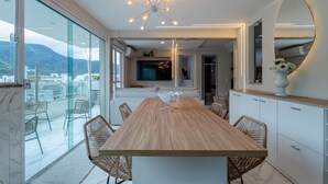 A modern dining area with a wooden table and wicker chairs, a large mirror, and a view of the outdoors. - Loft c Varanda Piscina e Academia em Itacuru (Mangaratiba)