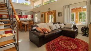 A spacious living area with a brown leather sofa, a red patterned rug, and a wooden staircase.