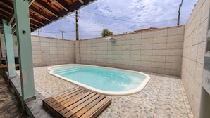 Ein Schwimmbecken mit Holzterrasse, Fliesenwänden und einem überdachten Bereich.