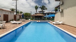 Une piscine entourée de bâtiments et de palmiers, avec des chaises longues et des parasols.