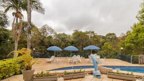Zona de piscina con sillas de descanso, sombrillas y plantas en macetas.