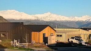 En modern byggnad med en träfasad och ett garage av metall framför, som ligger vackert placerad med snöklädda berg i bakgrunden under en klar himmel.