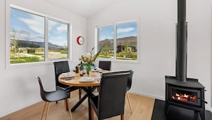 En matplats med ett runt bord, svarta stolar och utsikt över ett bergigt landskap genom stora fönster. En röd klocka sitter upphängd på väggen.