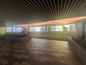 An indoor atrium with a patterned floor, a children's play area with swings, and a view of buildings through large windows. - Makati Biz District - Air Residence (Makati)