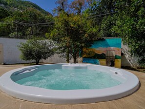 A hot tub in a backyard with a mural on the wall and trees around. - Casa em Itaipua u c Hidro e Churrasqueira - Maric (Marica)
