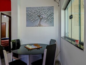 A dining area with a round table, four chairs, a chessboard, and a wall-mounted painting of a tree. - Casa em Itaipua u c Hidro e Churrasqueira - Maric (Marica)