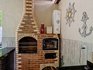 A brick-built oven with two windows, a red container, and decorative wall anchors. - Casa em Itaipua u c Hidro e Churrasqueira - Maric (Marica)