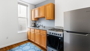 A compact kitchen with wooden cabinets, a stainless steel stove, and a refrigerator. - 𖡡 Jazz Suite - King Bed Studio 15 Min to NYC (Hoboken)