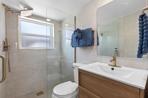 A modern bathroom with a glass-enclosed shower, a white toilet, and a vanity with a mirror. - Villa Bleu 1 (New Smyrna Beach)