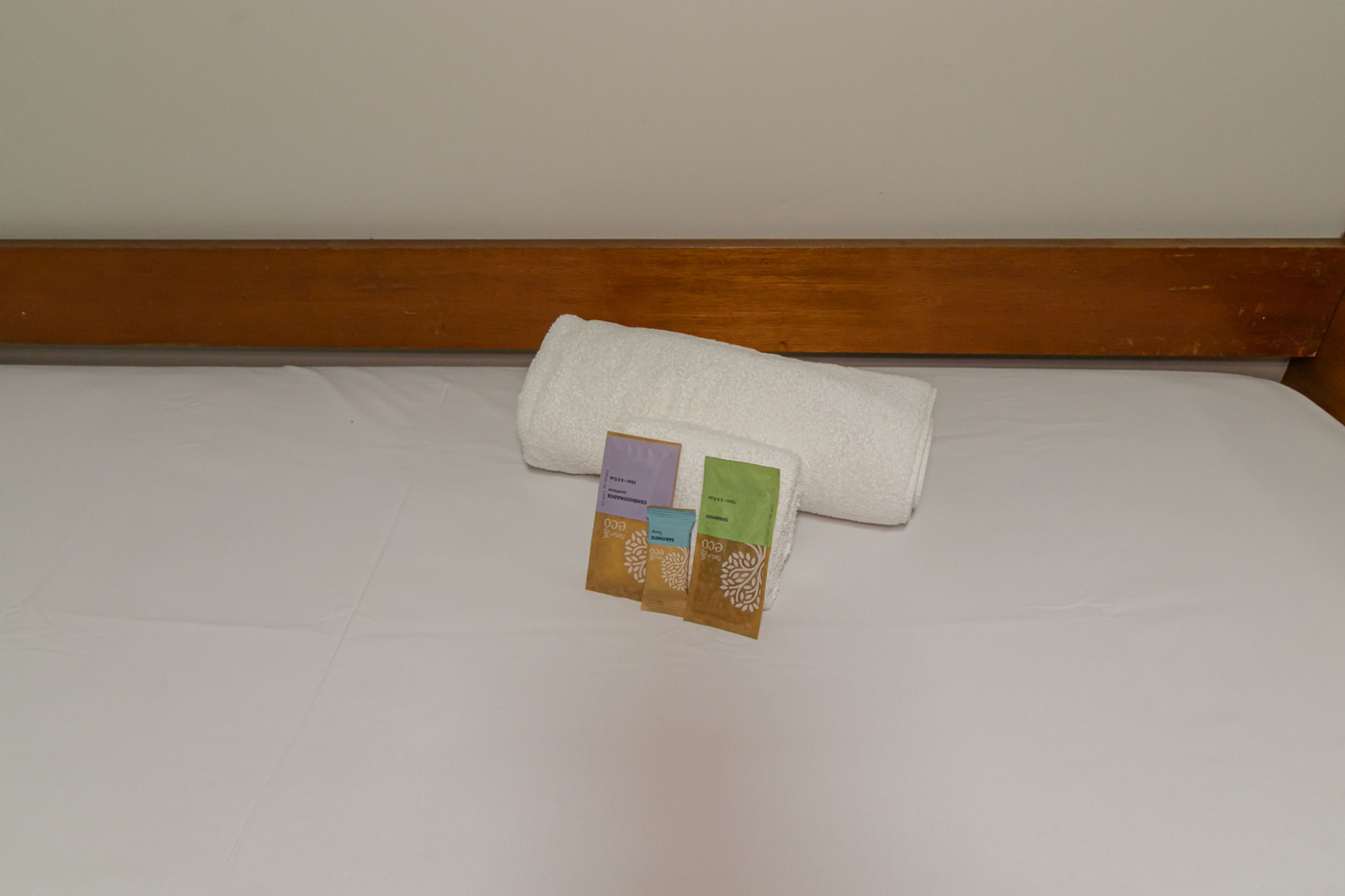 Un lit avec un drap blanc et une serviette blanche enroulée.