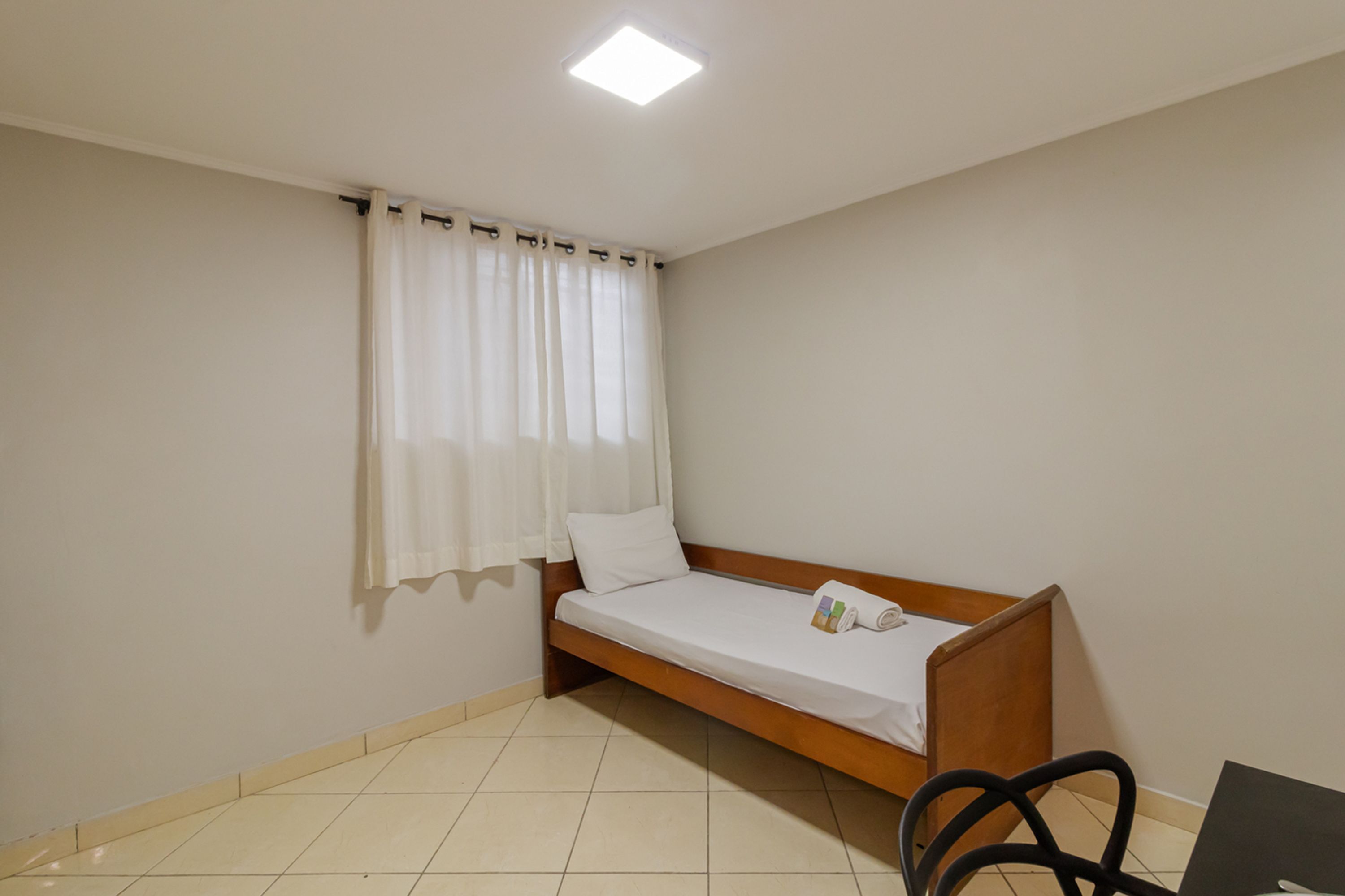A small, single-bed room with a wooden bed, a chair, and a desk.