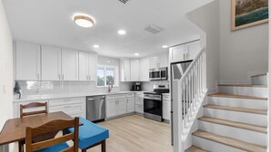 A modern kitchen with white cabinets, a dining table with chairs, a microwave, an oven, and a staircase with wooden steps. - Villa Bleu 3 (New Smyrna Beach)