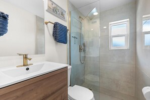 Een moderne badkamer met een witte wastafel, houten opbergmeubel en een douche met glazen wanden.