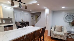 A modern kitchen with a marble countertop and wooden chairs, a dining area with a table and chairs, and a living room with a patterned sofa and a wall clock. - 3 Large Bedrooms | Modern Décor | Spacious (Everett)