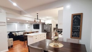 A modern kitchen with white cabinets, a central island, and a dining area with a dark wooden table and chairs. - 3 Large Bedrooms | Modern Décor | Spacious (Everett)