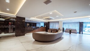A modern lobby with a curved seating area, a reception desk, and a large window with curtains. - Flat Beira-mar c Piscina e Academia em Mana ra (João Pessoa)
