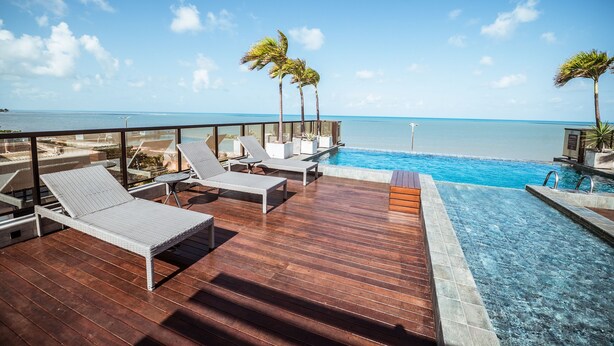 A poolside area with lounge chairs and a view of the ocean. - Flat Beira-mar c Piscina e Academia em Mana ra (João Pessoa)