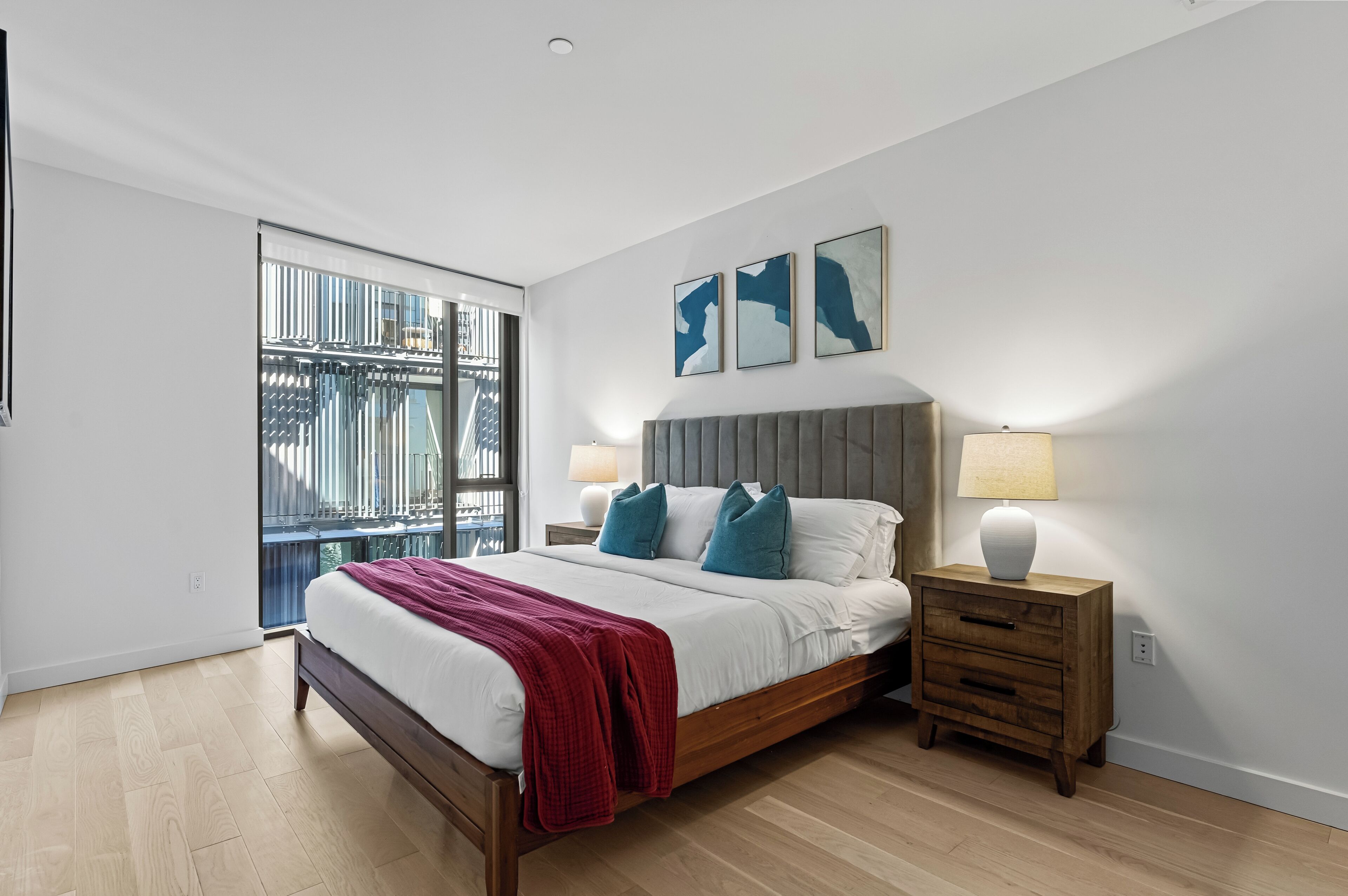 A modern bedroom with a large bed, two bedside tables, and a view of a cityscape through a sliding door.