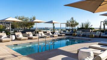 A poolside area with lounge chairs, umbrellas, and a view of the sea.