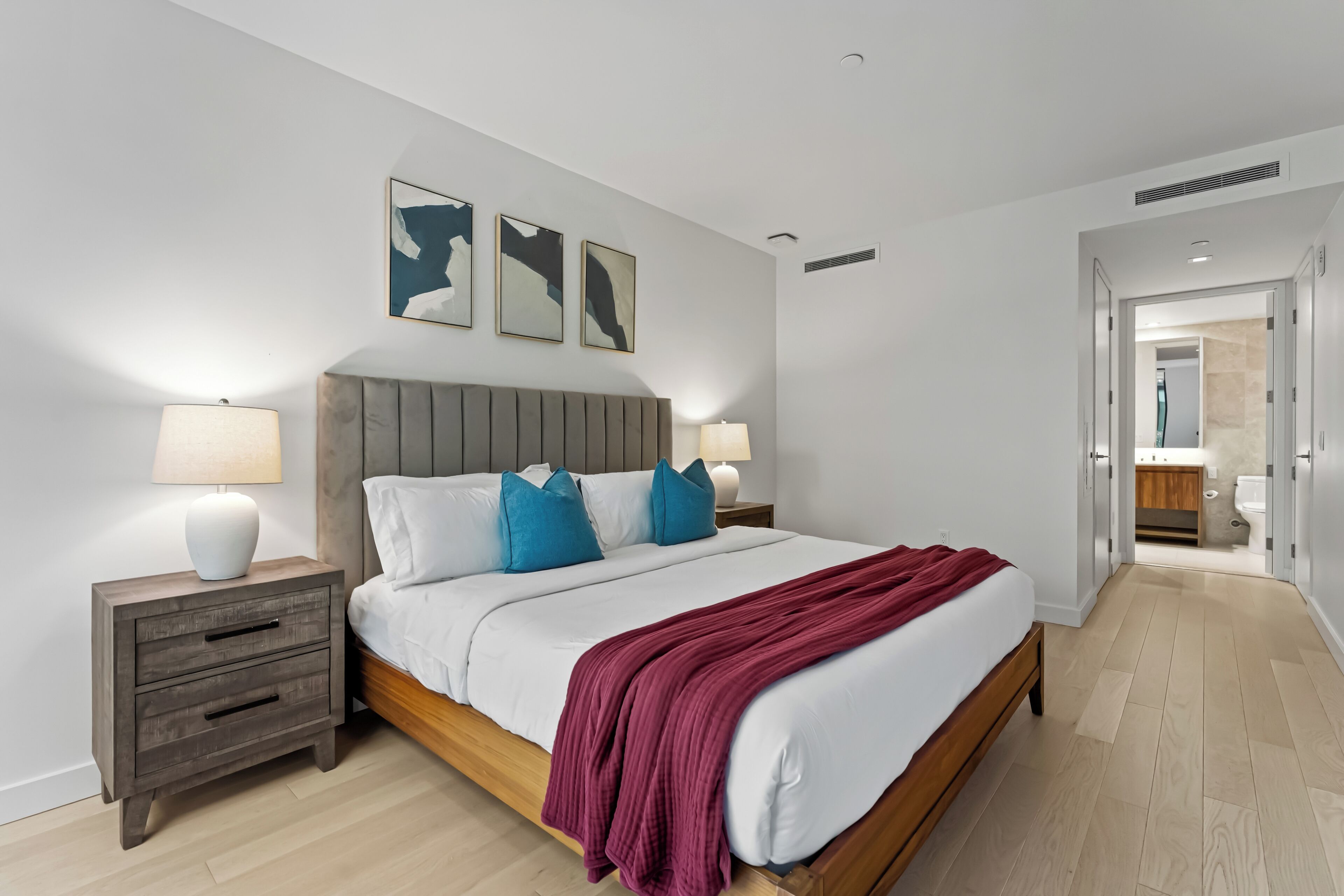 A modern bedroom with a wooden bed, white bedding, and two bedside tables with lamps.