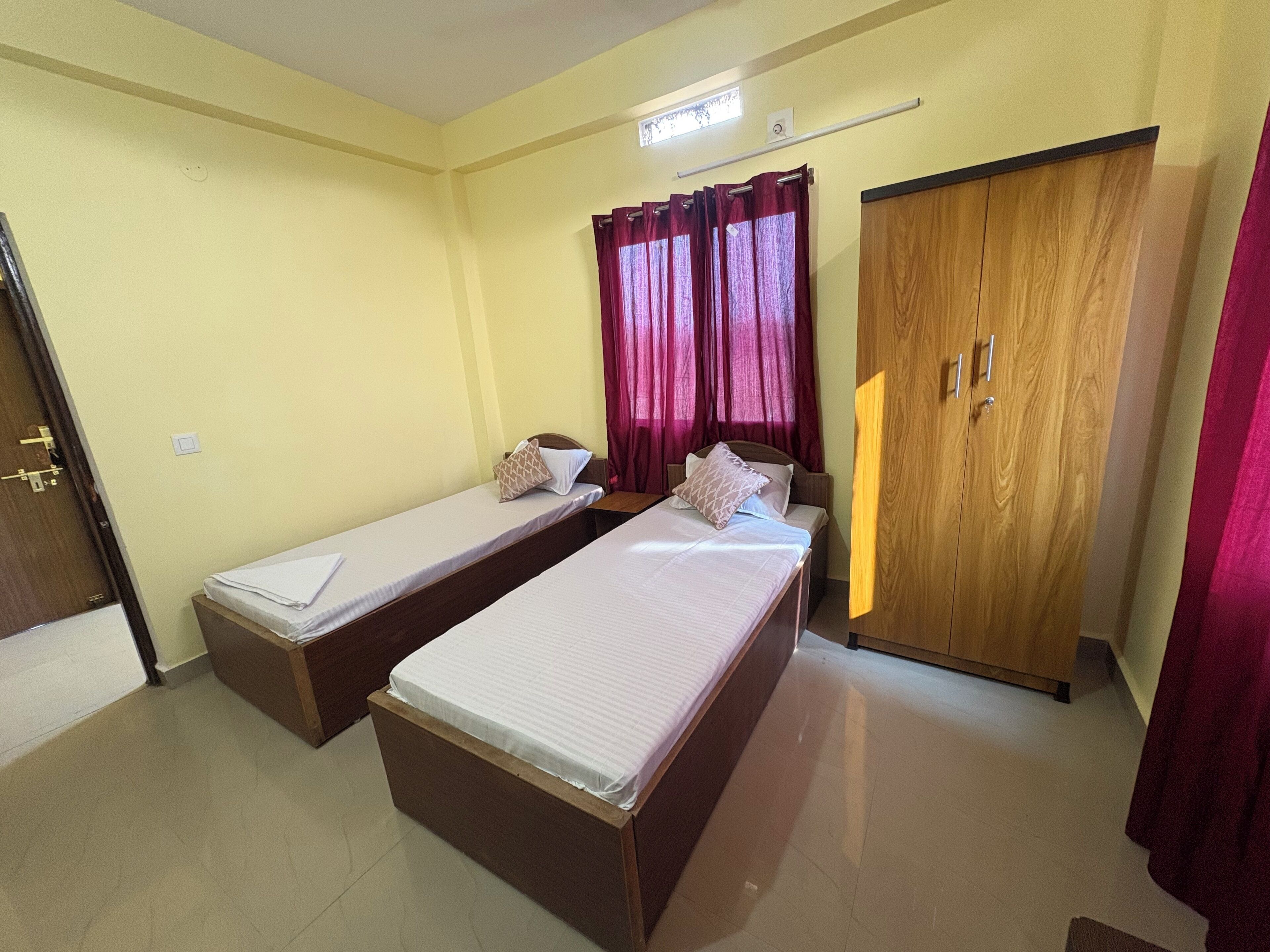 A room with two single beds, a wooden wardrobe, and a window with curtains.