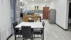 Cozinha compacta com área de refeições, com uma mesa de bancada de mármore, cadeiras de madeira e uma geladeira.