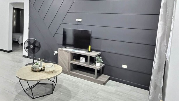 Uma sala de estar moderna com televisão de tela plana, ventilador de teto e mesa de centro de madeira.