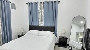 Um quarto moderno com uma cama grande, uma mesa de cabeceira, um espelho e um ventilador.