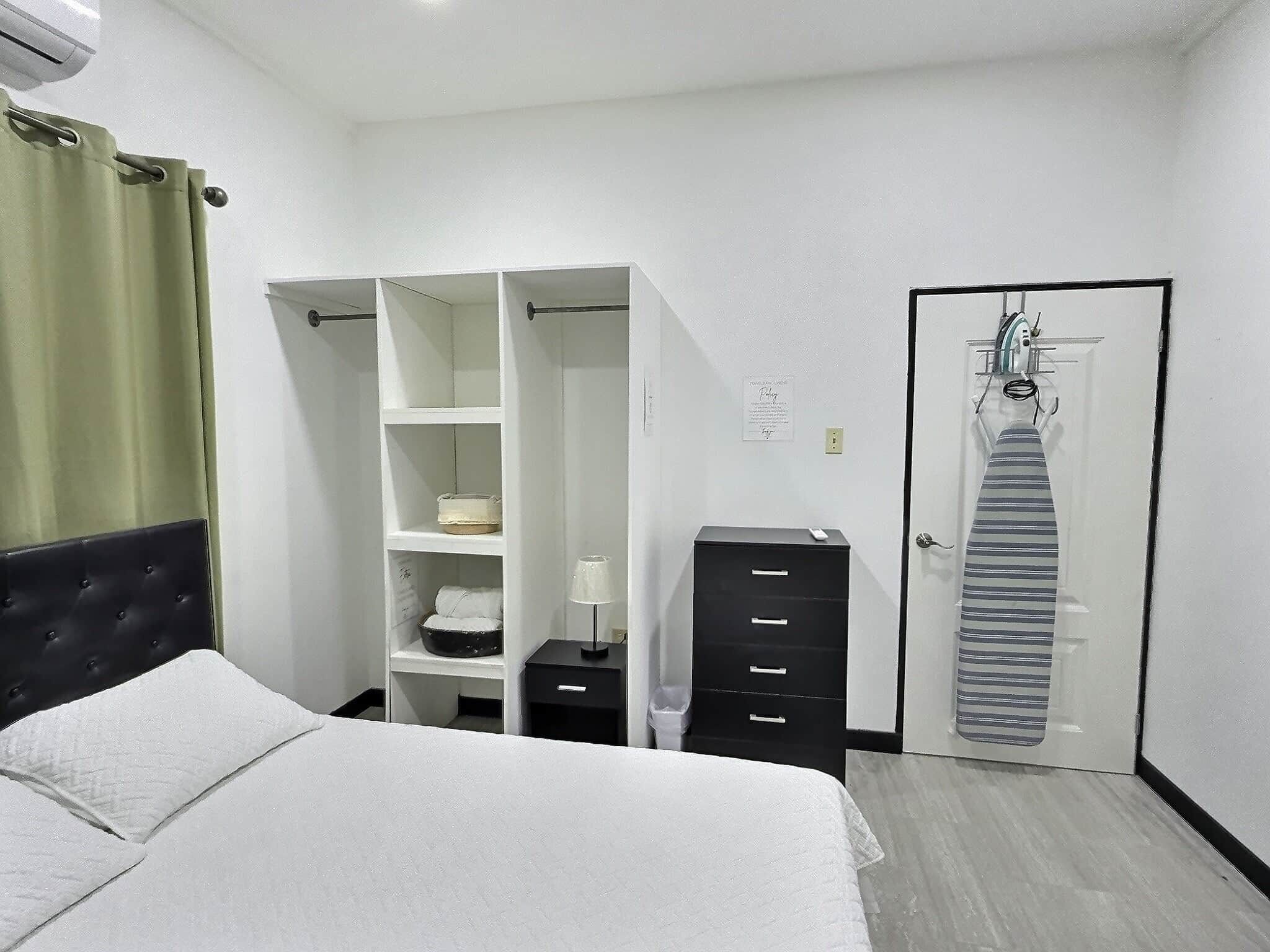 A bedroom with a bed, a wardrobe, a desk, and a door with a tie hanging on it.