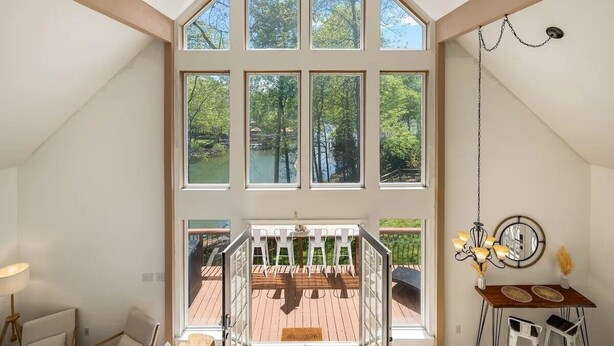 A spacious room with large windows, a wooden staircase, and a view of a deck and trees. - Spacious 4-bedroom 7 Beds waterfront cottage in lovely Mooresville, private dock (Mooresville)