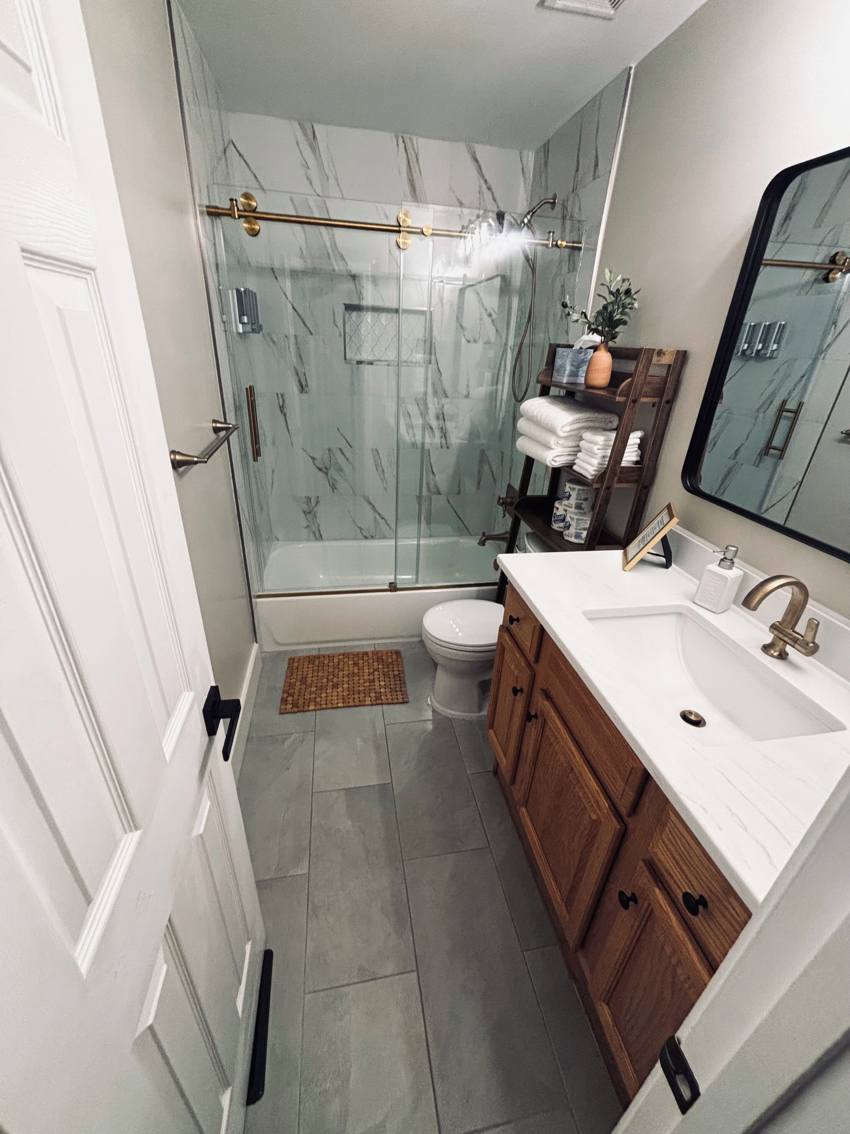 Une salle de bain avec une douche à parois de verre, des toilettes, un lavabo avec des meubles en bois et un miroir.