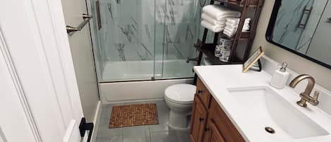 Une salle de bain avec une douche à parois de verre, des toilettes, un lavabo avec des meubles en bois et un miroir.