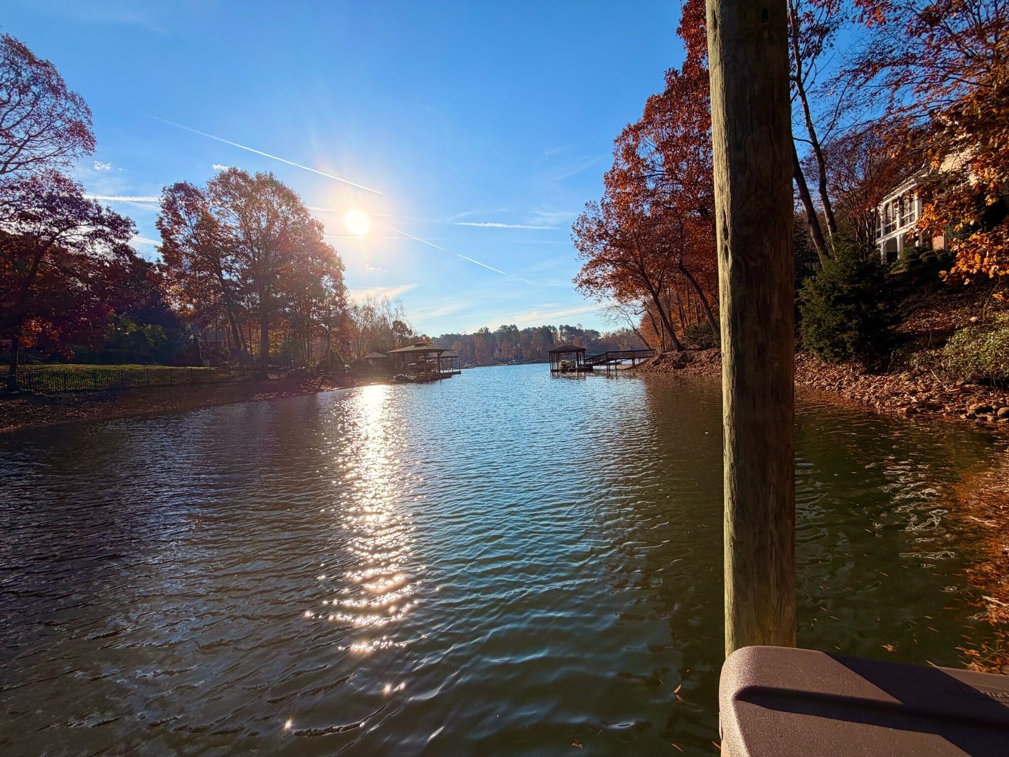 A river with a wooden dock and a gazebo, surrounded by trees with autumn foliage.