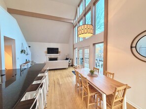 Amplia sala de estar con mesa de comedor, sillas, chimenea y ventanas grandes.