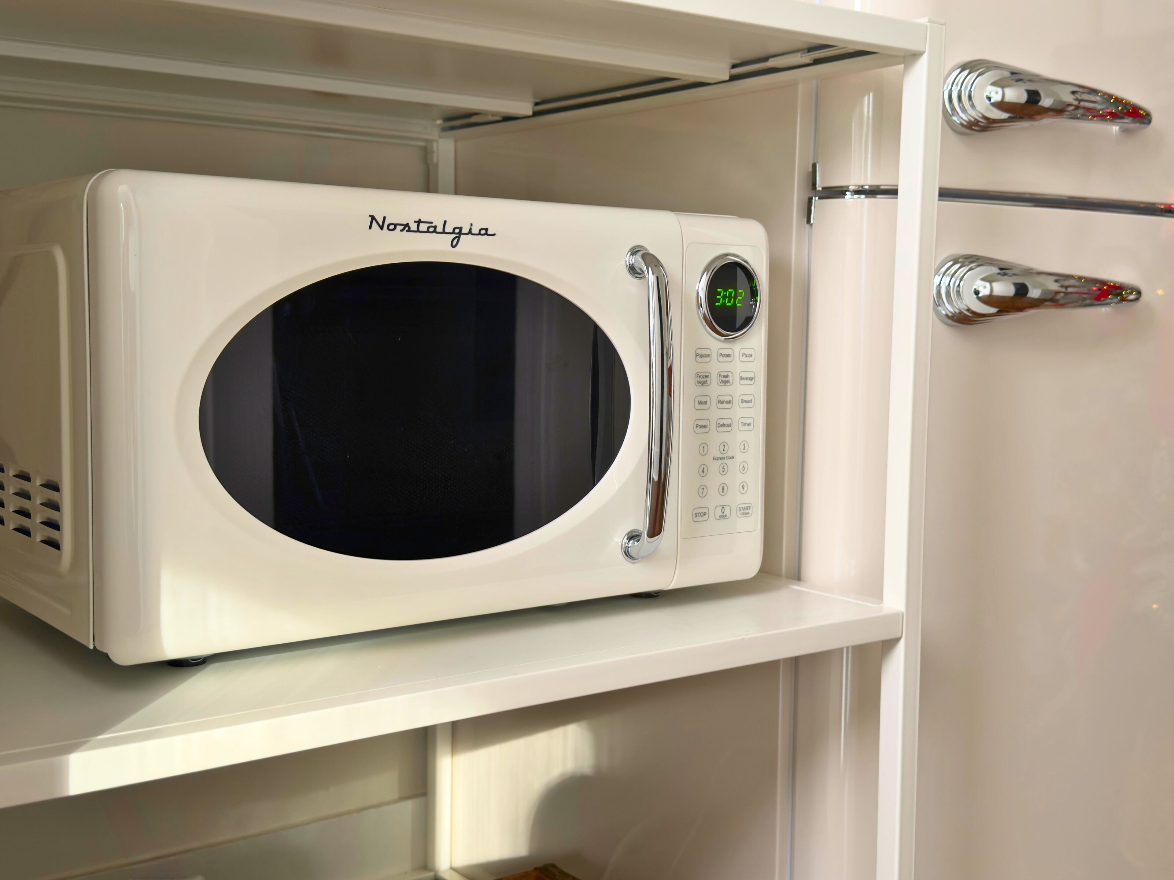 Un four à micro-ondes blanc, doté d’un écran numérique et d’un panneau de commande, est posé sur une étagère dans une cuisine.
