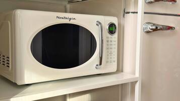 Un four à micro-ondes blanc, doté d’un écran numérique et d’un panneau de commande, est posé sur une étagère dans une cuisine.