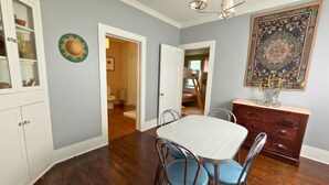 A dining area with a white table and blue chairs, wooden flooring, a white cabinet, and a decorative wall piece. - Boutique Historic Stay • Best Downtown Location (Savannah)