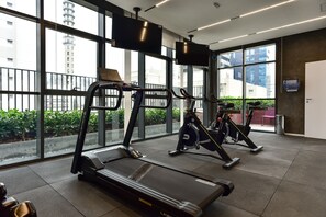 A gym with treadmills, elliptical machines, and a TV screen. - Studio Moderno c Academia a 800m do Metr Brooklin (São Paulo)