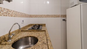 A kitchen with a granite countertop, stainless steel sink, white tiled backsplash, and a white refrigerator. - 05 Studio Prox Expo Berrini e Congonhas (São Paulo)