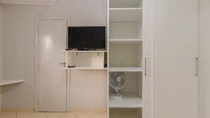A room with a closed door, a TV on a shelf, a standing fan, and a white wardrobe. - 05 Studio Prox Expo Berrini e Congonhas (São Paulo)