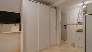 A compact kitchen with a flat-screen TV, a white wardrobe, and a tiled floor. - 05 Studio Prox Expo Berrini e Congonhas (São Paulo)