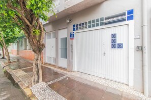 Zona residencial privada con un portón, una puerta de garaje blanca, un árbol pequeño y un camino de baldosas.