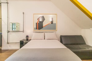Quarto moderno com cama, mesa de cabeceira, abajur, quadro abstrato emoldurado e janela com persianas.